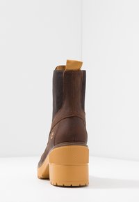 Hnědé kožené kotníkové boty s texturovanými bočními panely, žlutým poutkem a silnou gumovou podešví s vzorovaným designem.