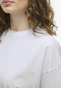 Camiseta de algodón blanca con escote redondo y mangas cortas, que presenta una textura suave y un diseño holgado. Vista en primer plano de la parte superior del cuerpo.