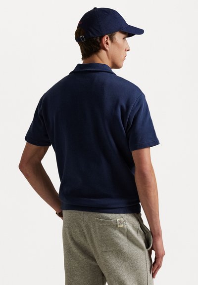 Navy blue polo shirt made of cotton, short sleeves, with a classic collar. Paired with light gray sweatpants featuring a back pocket.