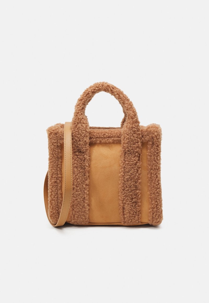 Petit sac cabas en daim beige avec bordure et poignées en peluche de style teddy, et une bandoulière réglable.