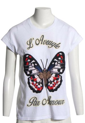 Camisa blanca de manga corta con una gran mariposa colorida y texto en francés "L' Aveugle Par Amour" en la parte delantera.