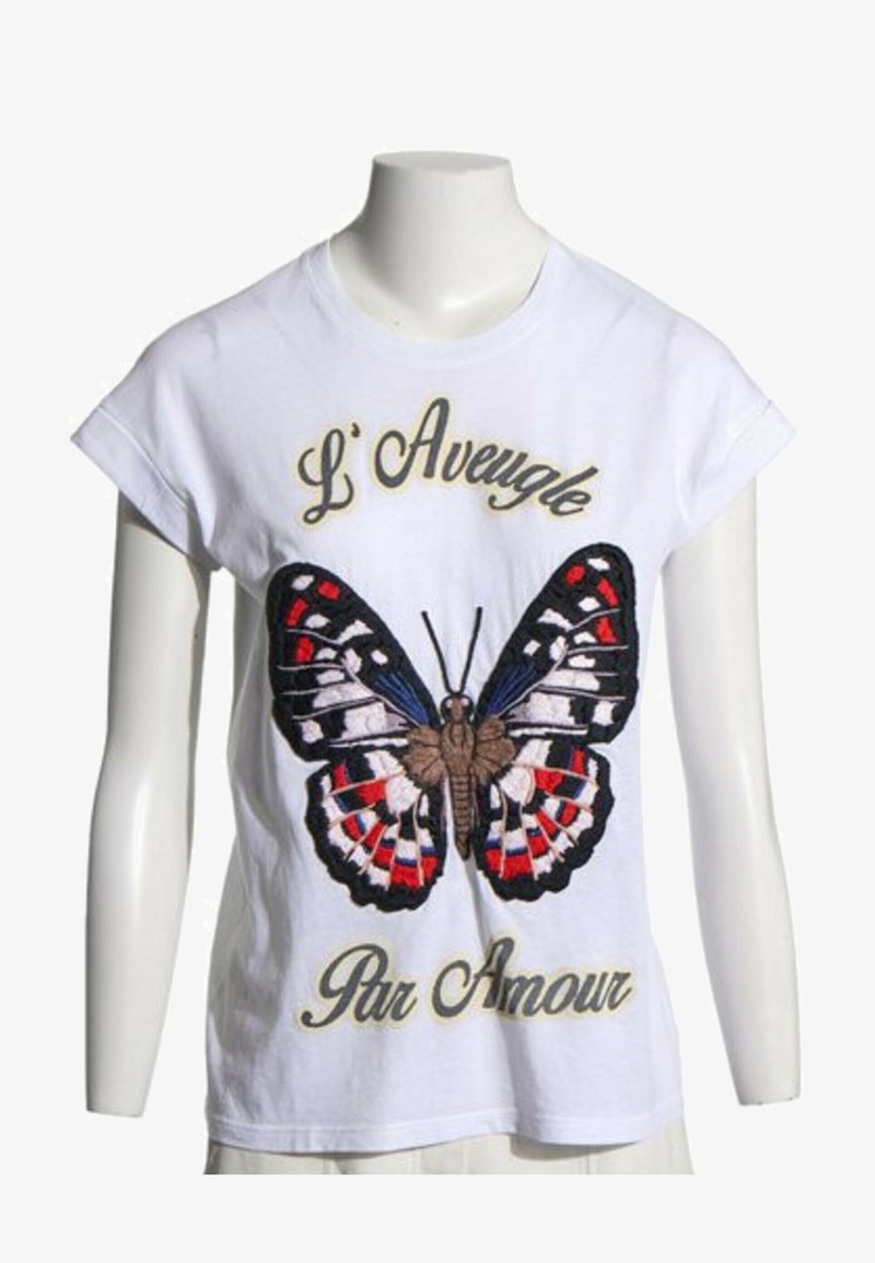Chemise blanche à manches courtes avec un grand papillon coloré et un texte en français "L' Aveugle Par Amour" sur le devant.