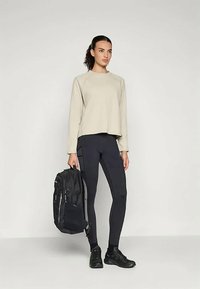 Heled pruun pikaaegne T-särk lühikese lõikega, sobitatud mustade legginsitega ja musta seljakotiga. Minimalistlik ja funktsionaalne välimus.