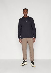 Schwarzer Sweatshirt mit kleinem weißem Logo, beige Jogginghose und schwarz-weißen Turnschuhen. Lässiger Stil, weiches Material, lockere Passform.