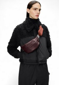 Schwarze strukturierte Jacke mit cropped Design, ausgestattet mit einer burgunderfarbenen Umhängetasche und einem kleineren orangefarbenen Beutel, der mit metallischen Beschlägen befestigt ist.
