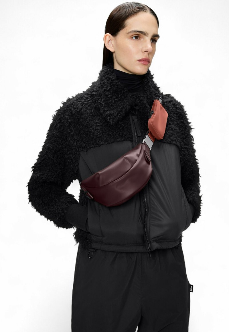 Schwarze strukturierte Jacke mit cropped Design, ausgestattet mit einer burgunderfarbenen Umhängetasche und einem kleineren orangefarbenen Beutel, der mit metallischen Beschlägen befestigt ist.