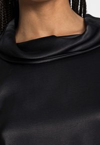 Musta kangas toppi, jossa on leveä, roikkuva pääntie ja sileä tekstuuri, hienovaraisella kiillolla ja ilman näkyviä kuvioita tai koristeita.