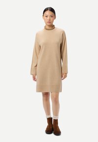 Robe-pull beige à manches longues et col montant, fabriquée dans un matériau doux ; associée à des bottines marron et des chaussettes crème.