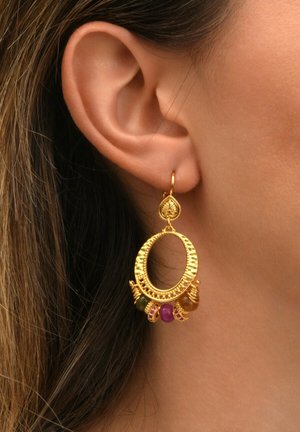 Gros plan sur une oreille portant une boucle d'oreille en or avec un design texturé et cinq charms en pierres colorées suspendus en bas.