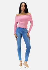 Rippenshirt, schulterfrei, rosa Pullover mit langen Ärmeln, kombiniert mit hellblauen Skinny Jeans und weißen spitzen Schuhen.