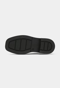 Talpă de pantof din cauciuc negru, cu o suprafață texturată ce prezintă multiple secțiuni striate pentru aderență și stabilitate. Design plat cu o formă rotunjită.