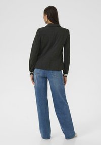 Blazer gris ajusté au design cintré, avec des poignets rayés, associé à un jean bleu à jambes larges. Texture lisse et silhouette structurée.