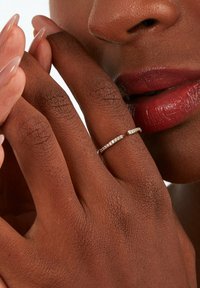 Anello in argento delicato con un design ondulato, adornato con piccole pietre preziose trasparenti, mostrato su una mano con unghie curate e pelle dalle texture.