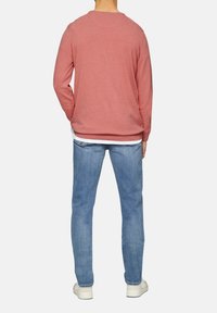Rood gebreid sweater, ronde hals, lange mouwen, gecombineerd met lichtblauwe jeans en witte sneakers, gezien van achter.