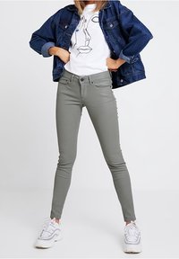 Šedé slim-fit džíny v kombinaci s bílým tričkem s liniovým kreslením a modrou denimovou bundou, doplněné bílými teniskami.