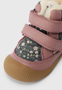 Sapatinho de couro rosa para criança com tecido floral, fechos de Velcro duplos, forro felpudo e sola de borracha castanha texturizada.