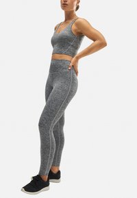 Top deportivo corto gris y leggings de cintura alta con costuras en contraste. Tela suave, diseño ceñido al cuerpo y combinado con zapatillas deportivas negras.