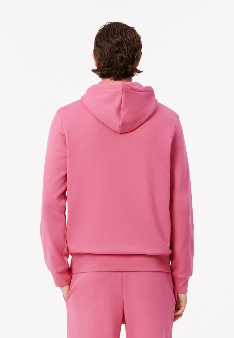 Felpa rosa con cappuccio, realizzata in tessuto morbido. Presenta polsini e orlo a coste, texture liscia e un design a vestibilità rilassata.