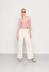 Top cropped rosa com estampa floral e alças finas, combinado com calças largas de cintura alta em creme e sandálias brancas.