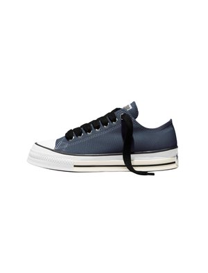 Zapatilla baja de lona azul marino con suela de goma blanca, cordones negros y detalle de raya negra en el lateral de la suela.