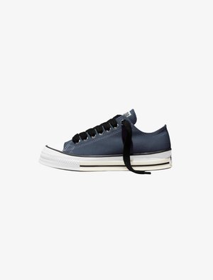 Low-top navy blue canvas sneaker with white rubber sole, black laces, and black stripe detail on side of sole.
