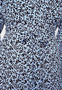 Modré šaty s černým vzorem listů, se zavázaným páskem v pase a dlouhými rukávy, vyrobené z lehkého materiálu.