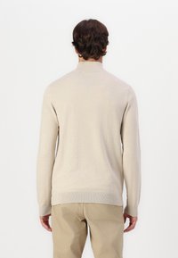 Suéter de punto beige con mangas largas, cuello alto y puños acanalados. Textura suave, forma ajustada y un diseño limpio sin estampados.
