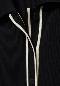 Polo negro acanalado con una tapeta blanca en contraste, tres botones negros y una tela texturizada.