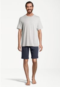 Grå bomulds t-shirt med korte ærmer og rund hals, parret med marineblå bomulds shorts. Modellen står barfodet på en enkel baggrund.