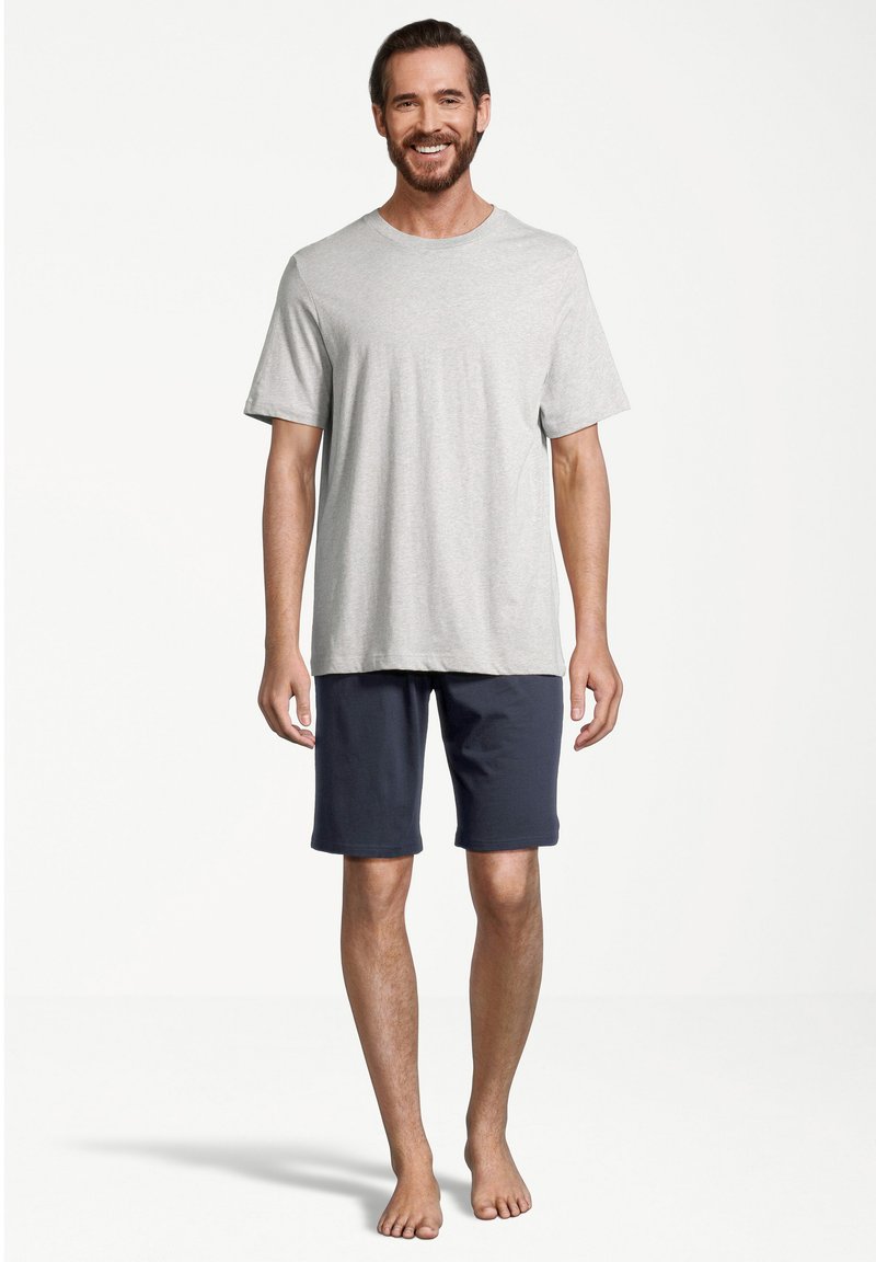 Graues Baumwoll-T-Shirt mit kurzen Ärmeln und Rundhalsausschnitt, kombiniert mit navyblauen Baumwollshorts. Das Model steht barfuß vor einem schlichten Hintergrund.