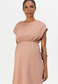 Maternity dress in soft pink fabric, featuring short sleeves, an elastic waist, and a flowing silhouette. Smooth texture and casual design.