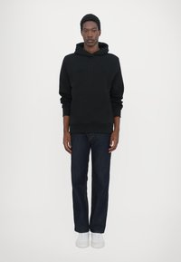 Black hoodie with front pocket and embossed "QUARTZ CO" logo, paired with dark blue jeans and white sneakers. Smooth fabric texture.