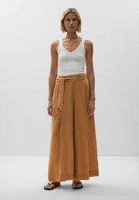 Tan wide-leg trousers with a tied waistband, paired with a white tank top. The fabric appears soft and textured, suitable for casual wear.
