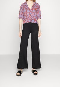 Beskuvad lila blus med röd abstrakt tryck, parat med svarta vida byxor och svarta platåsandaler. Slät tyg, avslappnad passform.