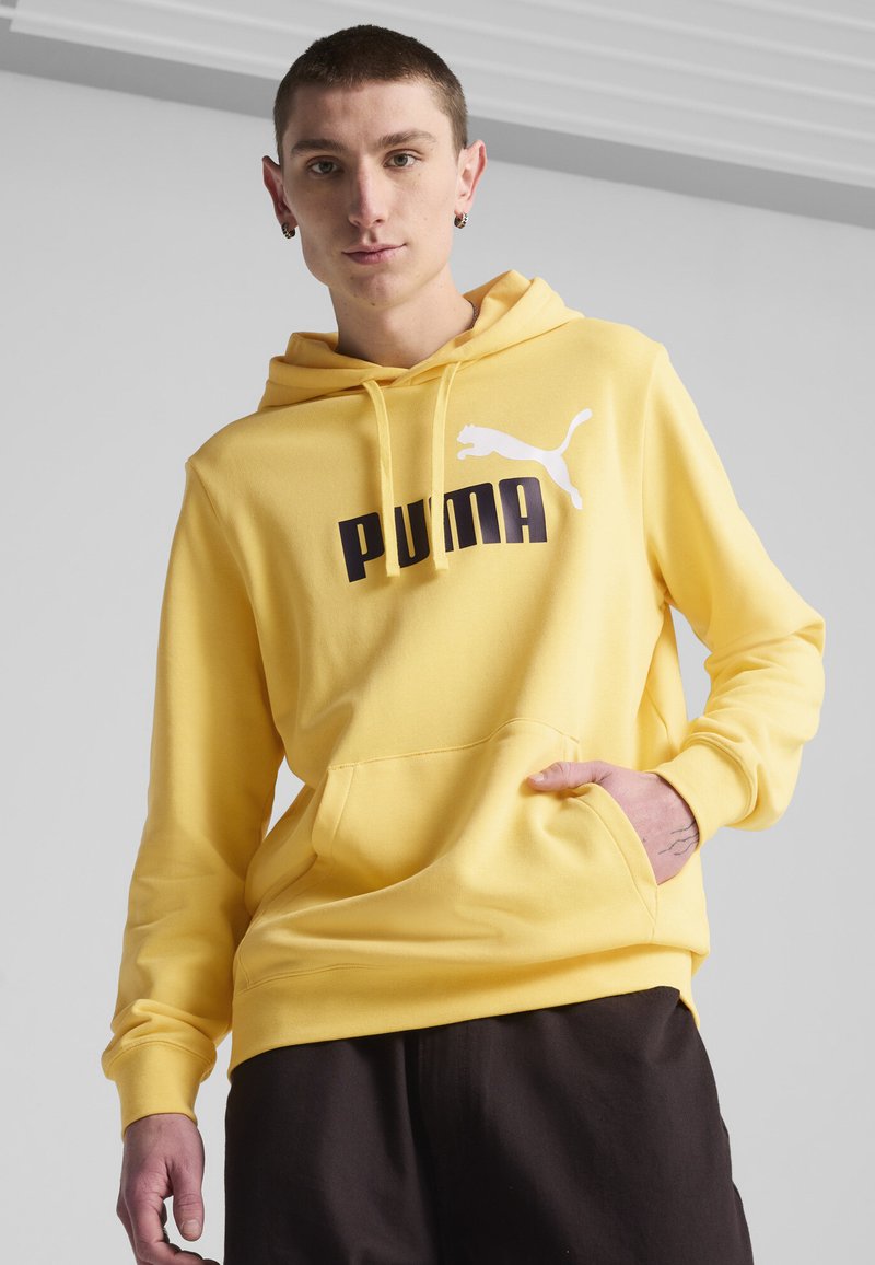 Felpa gialla con cappuccio, caratterizzata da un logo Puma bianco e testo nero. Tessuto morbido, con tasca frontale e polsini a coste per un look aderente.