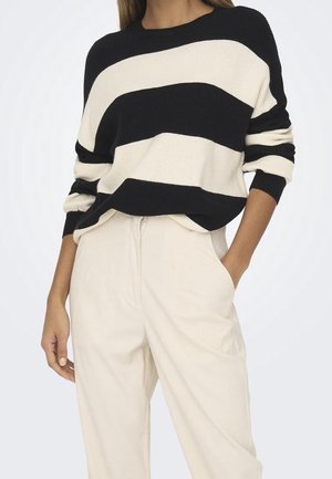 Maglione a righe nero e crema realizzato in maglia con una texture a coste, dotato di maniche larghe e vestibilità rilassata, abbinato a pantaloni crema.
