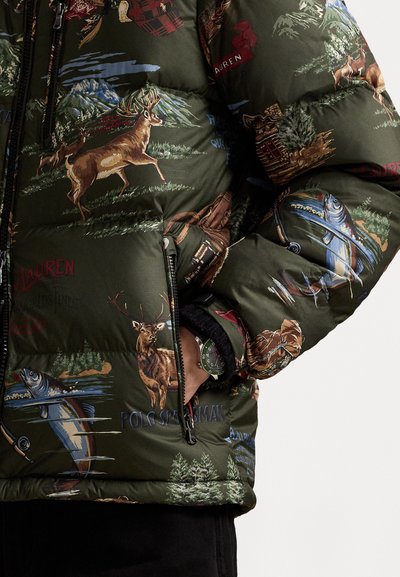 Green puffer jacket with nature-themed print of deer, fish, trees, mountains, and fishing gear, worn with hand in zippered pocket.
