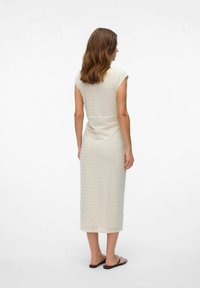 Robe beige clair jusqu'au genou avec des manches courtes, motif en zigzag texturé et taille cintrée, assortie à des tongs noires.