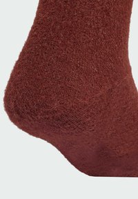 Hnědá, texturovaná ponožka s chlupatým vzhledem, ukazující patu a pletený vzor. Měkká látka poskytuje silný, teplý vzhled.