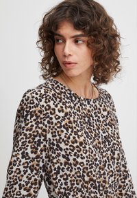 Šaty s leopardím motívom z ľahkého materiálu; majú okrúhly výstrih a dlhé rukávy; farby zahŕňajú krémovú, čiernu a hnedú.