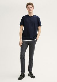 Camicia henley blu navy a maniche corte con superficie strutturata, abbinata a pantaloni fitted grigio scuro e scarpe stringate nere.