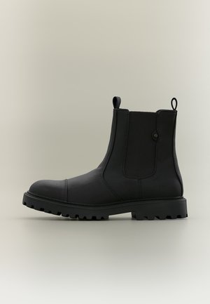 Bottine noire en cuir avec panneaux latéraux élastiques, languettes à l'avant et à l'arrière, et semelle épaisse à crampons pour une bonne adhérence.