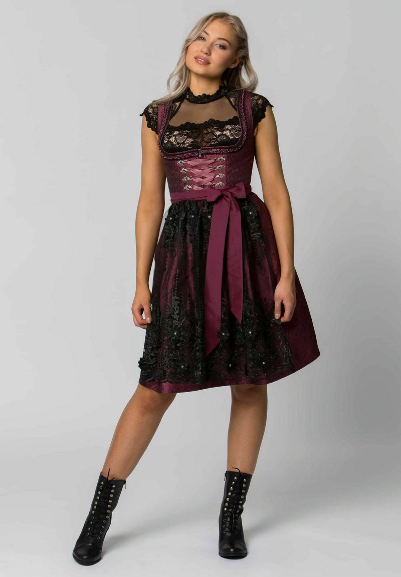 Burgunderrotes, besticktes Kleid mit taillierter Oberseite, Spitzenakzenten und ausgestelltem Rock. Betont mit einem satinierten Band in der Taille und schwarzen Stiefeln.