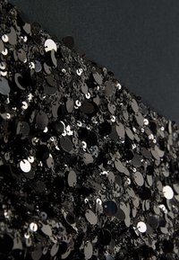 Tela negra de lentejuelas con lentejuelas circulares y en forma de disco, que reflejan la luz y están dispuestas de forma densa sobre un fondo negro suave.