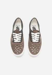 Brune suedesneakers med hvite snørebånd, svarte detaljer og sølvnagler på tåområdet. Gummisåle og klassisk logo på innersålen.