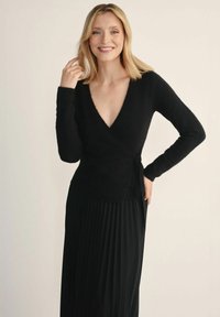 Czarny sweter o kroju kopertowym z głębokim dekoltem w kształcie litery V i długimi rękawami, wykonany z miękkiego, teksturowanego materiału, zestawiony z plisowaną czarną spódnicą.