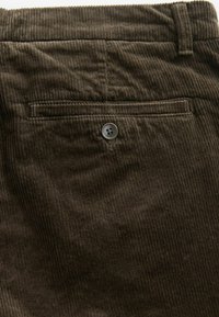 A barna corduroy nadrágok texturált felszínnel rendelkeznek, függőleges bordázattal, egy gombos hátsó zsebbel és egyenes szabású dizájnnal készültek.