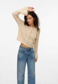 Pull court beige clair avec tricot texturé et devant à boutons, porté avec un jean bleu taille haute au fit décontracté.