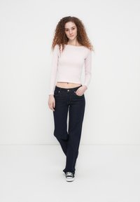 Ροζ ανοιχτό ροζ crop top με μακριά μανίκια, συνδυασμένο με σκουρόχρωμα τζιν με ίσια γραμμή και κλασικό σχέδιο με πέντε τσέπες. Μαύρα αθλητικά παπούτσια ολοκληρώνουν το ντύσιμο.