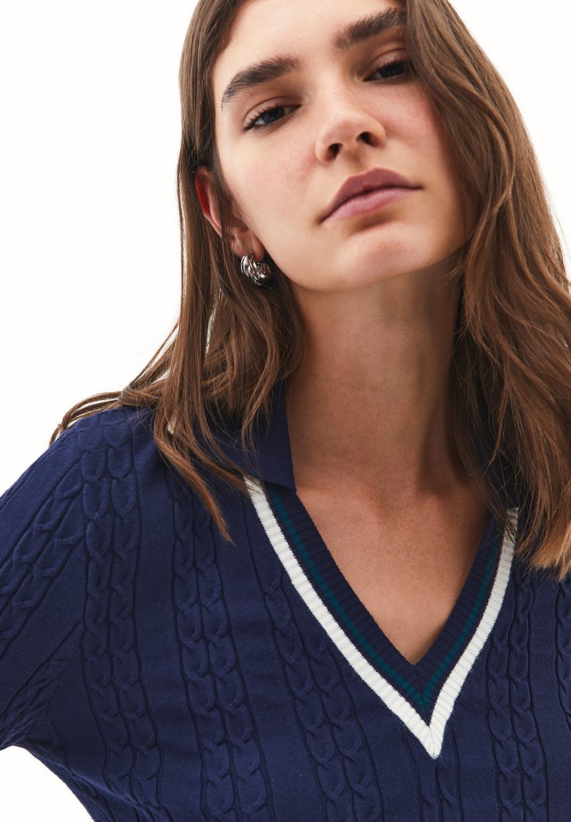 Suéter de punto navy con un diseño de cable texturizado, escote en V y un cuello acanalado de colores blanco y verde azulado.